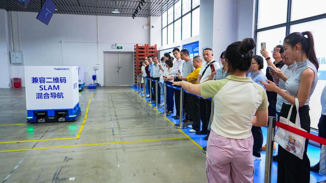 走访团在塔斯克机器人有限公司观摩智能托盘机器人工作场景。