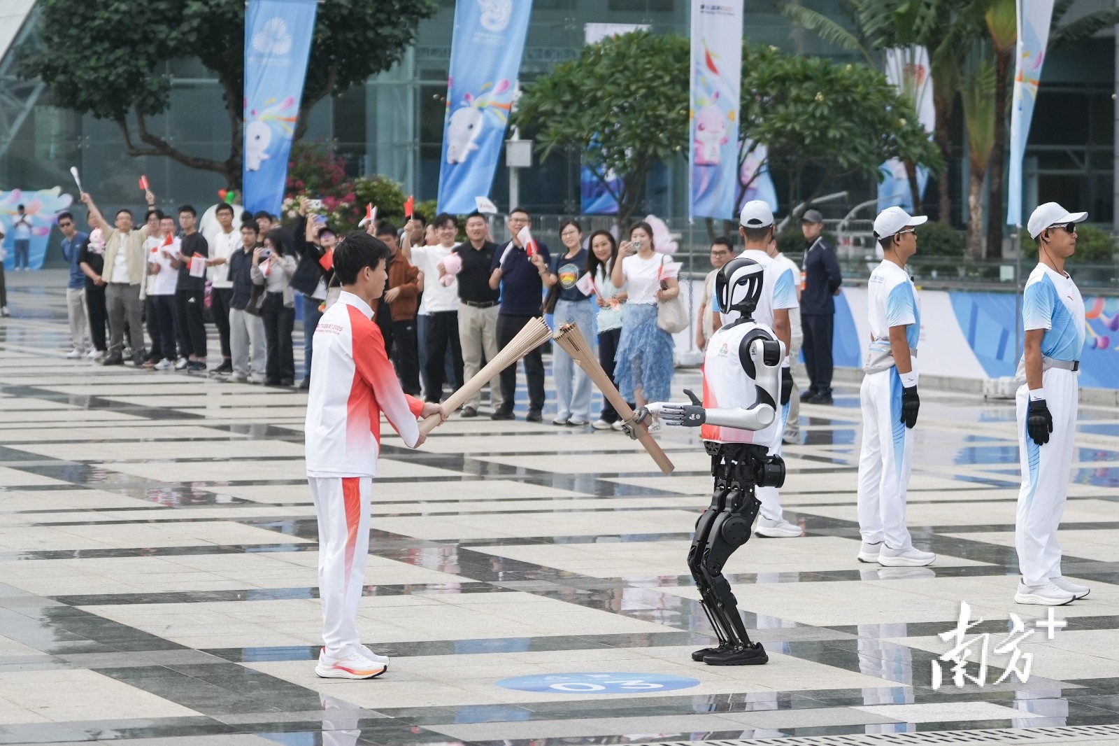 第十五届全国运动会深圳站火炬传递活动现场,“0号”火炬手人形机器人“夸父”向“手搓火箭”的高中生王裕宁传递火炬